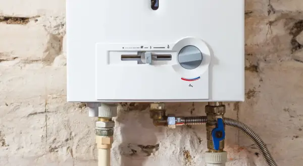 Detalle de una caldera mixta blanca con controles y tuberías conectadas a una pared de ladrillo.