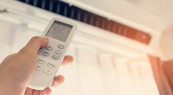 Mano ajustando el control remoto de un aire acondicionado para disfrutar de unas agradables frigorías.