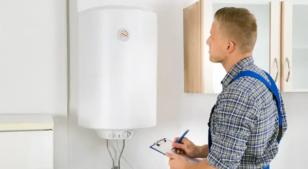 Técnico revisa un termo eléctrico blanco, anotando en una libreta.