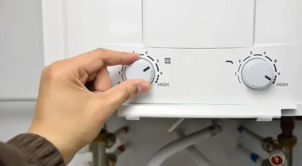 Mano ajustando el dial de temperatura de un termo eléctrico. Se acerca el momento de desmontar el termo eléctrico para su mantenimiento.