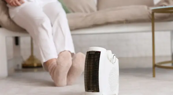 Persona sentada con calcetines gruesos, disfrutando del calor de un calefactor portátil, el mejor sistema de calefacción para un piso.