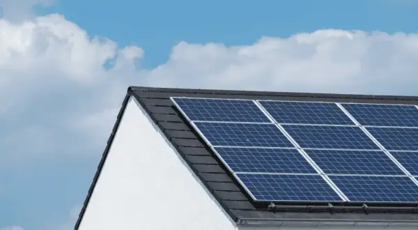 Paneles solares en tejado de casa blanca, bajo un cielo azul con nubes. ¿Cuántas placas solares necesito para una casa?