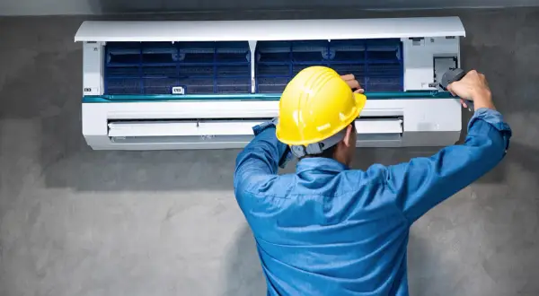 Técnico con casco amarillo ajusta un aire acondicionado, buscando reducir los decibelios del aire acondicionado para un ambiente más silencioso.