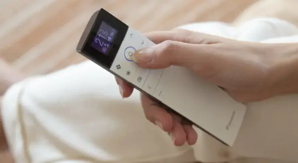 Mano ajustando el control remoto de un cool aire acondicionado a 21 grados.