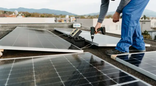 Instalación de un panel solar para aire acondicionado en una azotea. Un técnico usa un taladro para fijar el panel.