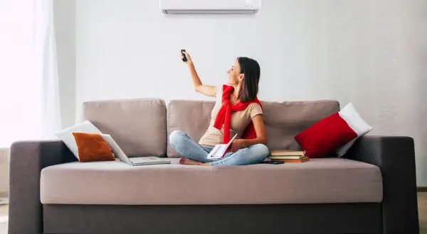 Mujer sentada en sofá, usando control remoto para ajustar uno de los tipos de aire acondicionado.
