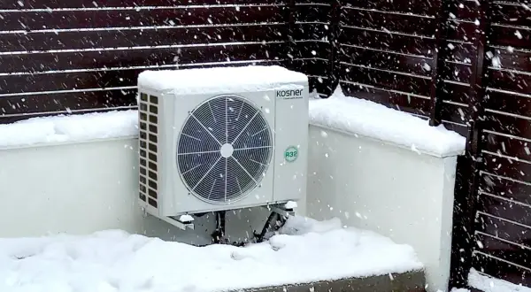 Unidad exterior de bomba de calor Kosner cubierta de nieve, mostrando su capacidad para mantener la temperatura en invierno.