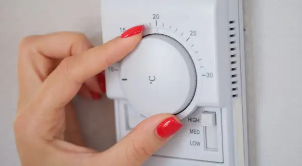Mano ajustando el termostato para decidir a qué temperatura poner la calefacción en invierno. Se ve el dial con números y la opción de intensidad.