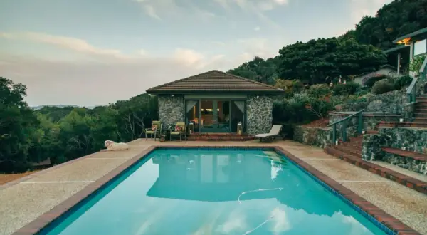 Piscina con agua cristalina, rodeada de vegetación y una casa de piedra. Ideal para climatizar piscina y disfrutar todo el año.