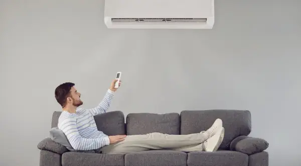 Hombre relajado en sofá, usando control remoto para que el aire acondicionado renueve el aire y refresque la estancia.