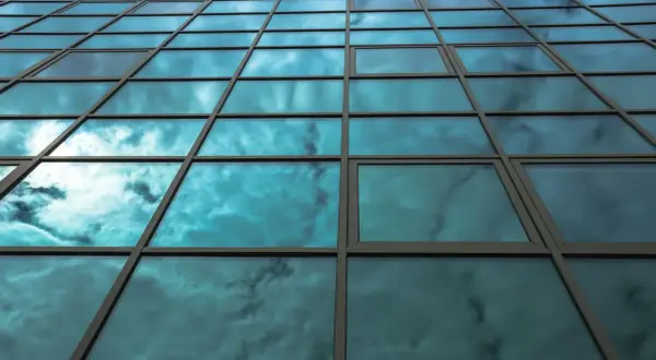Fachada de edificio con cristales fotovoltaicos reflejando un cielo nublado y azul.