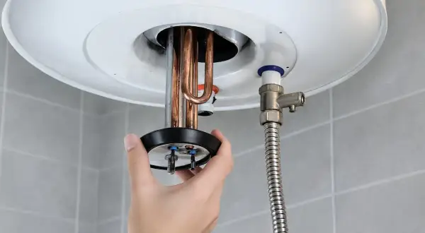 Mano retirando resistencia de termo eléctrico. ¿Cuánto tarda en vaciarse un termo eléctrico de 80 litros?