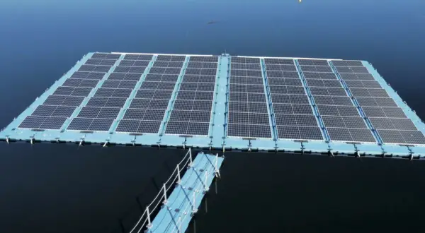 Plataforma de energía fotovoltaica flotante sobre un cuerpo de agua azul, con un pasarela azul conectada.