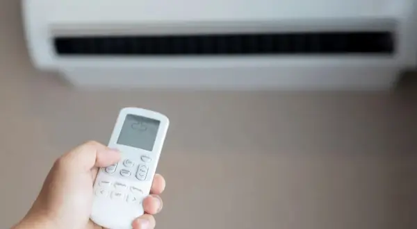 Mano sujetando control remoto de aire acondicionado para combatir el calor. La pantalla muestra 25 grados.