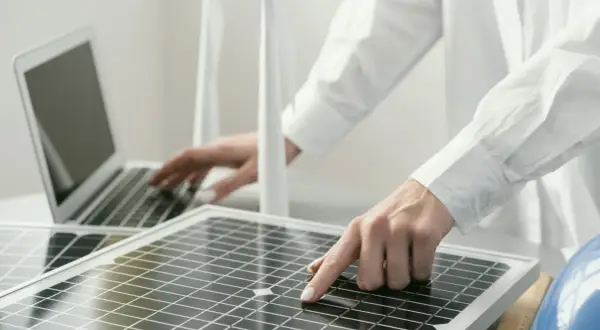 Persona revisa placas solares mientras trabaja en una laptop.