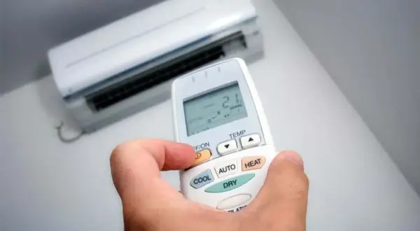 Mano sujetando control remoto de aire acondicionado, ajustando modo deshumidificador.