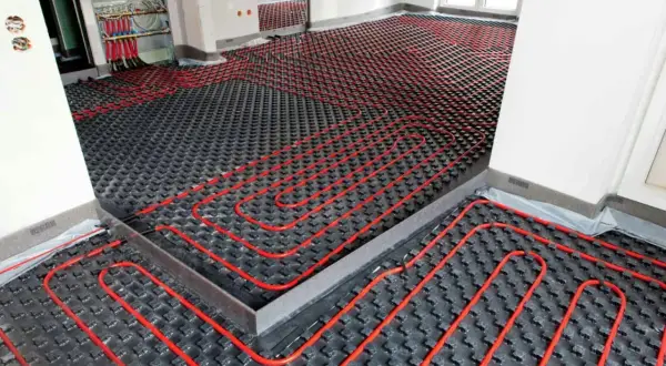 Instalación de sistema de calefacción por suelo radiante, con tuberías rojas sobre paneles negros. La temperatura del suelo radiante se controla desde un colector.