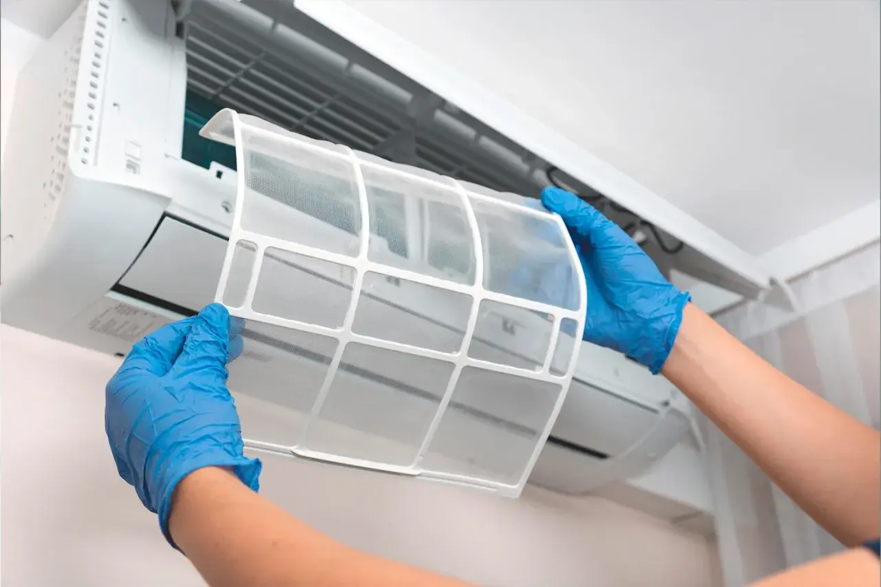 Manos con guantes azules retiran filtro de aire acondicionado. El mantenimiento es clave para saber cuanto dura un aire acondicionado.