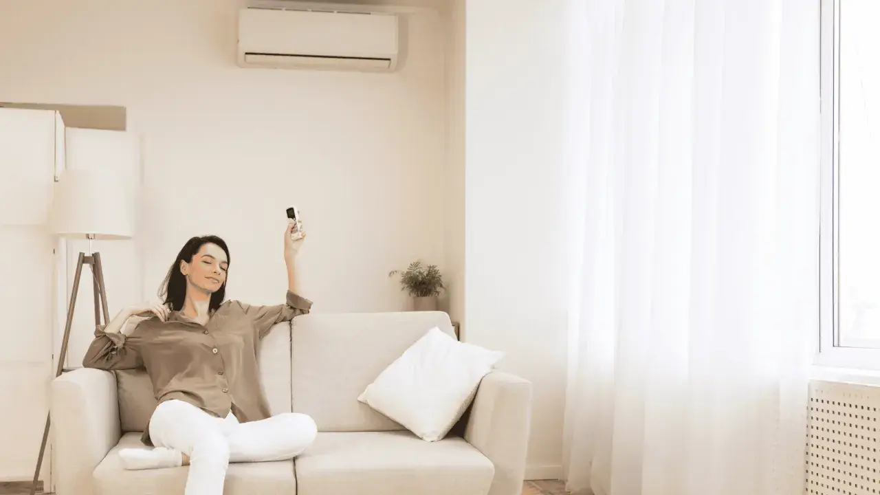 Mujer relajada en sofá con control remoto, pensando cuántas frigorías para 30 metros cuadrados necesita su hogar.