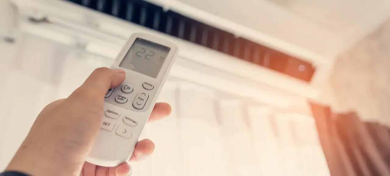 Mano ajustando el control remoto de un aire acondicionado para disfrutar de unas agradables frigorías.