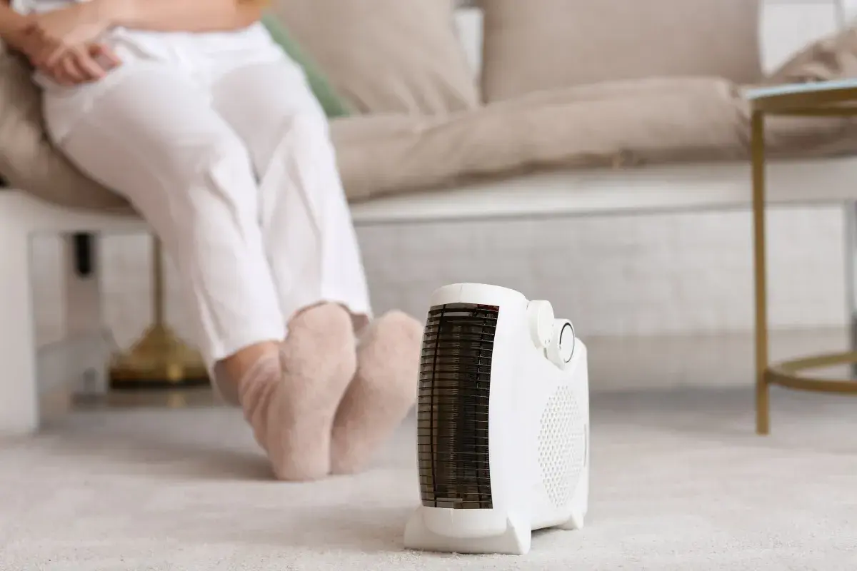 Persona sentada con calcetines gruesos, disfrutando del calor de un calefactor portátil, el mejor sistema de calefacción para un piso.