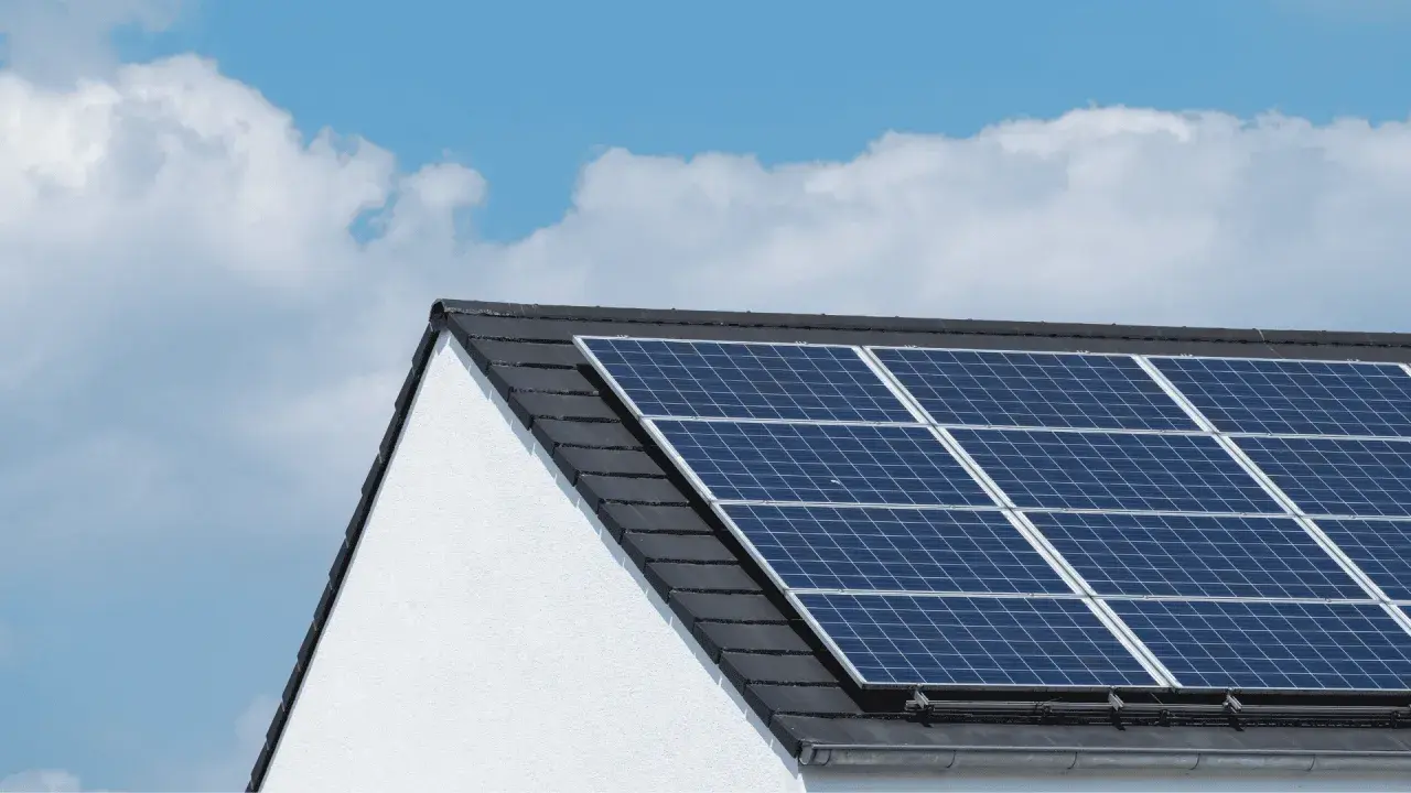 Paneles solares en tejado de casa blanca, bajo un cielo azul con nubes. ¿Cuántas placas solares necesito para una casa?