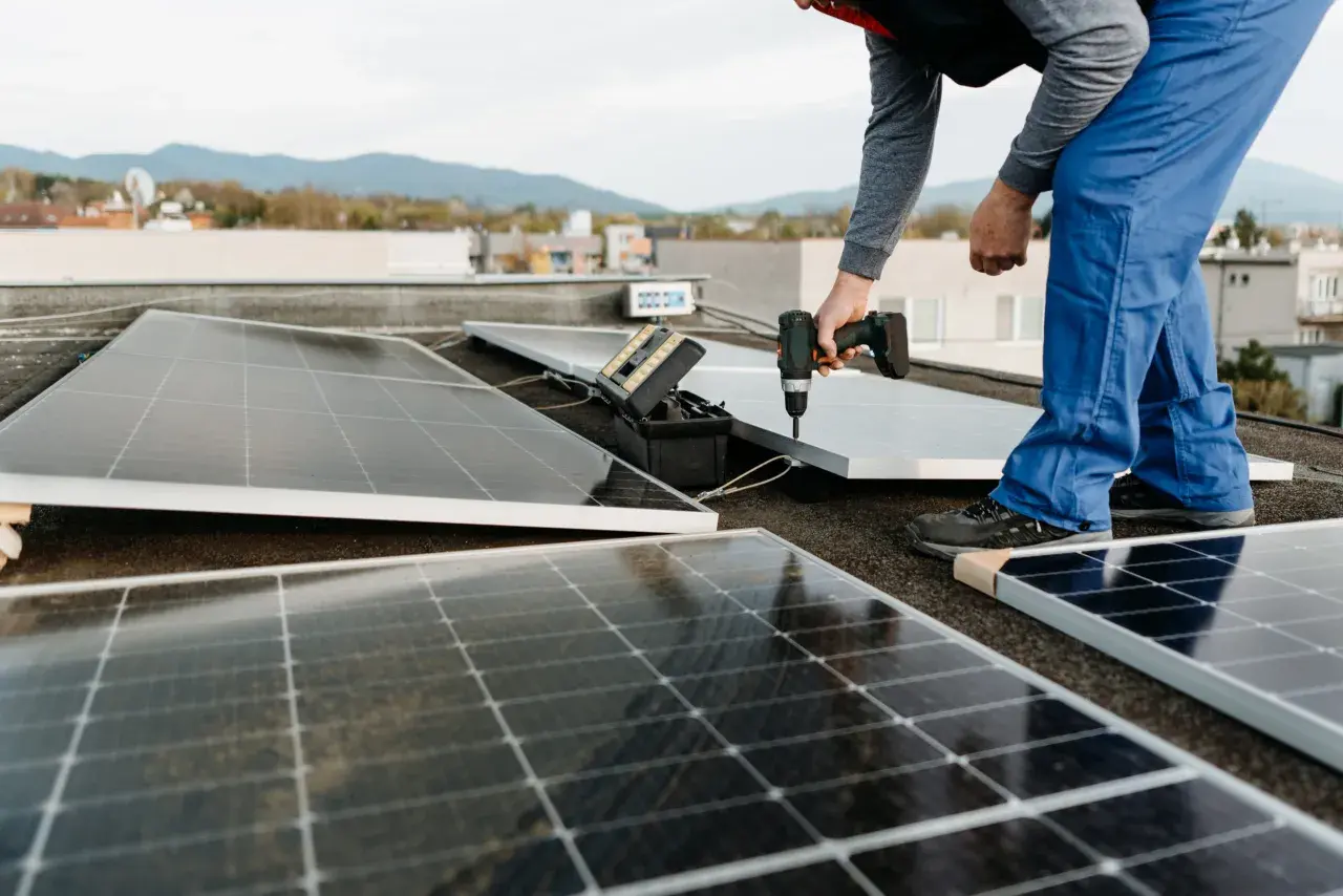 Instalación de un panel solar para aire acondicionado en una azotea. Un técnico usa un taladro para fijar el panel.