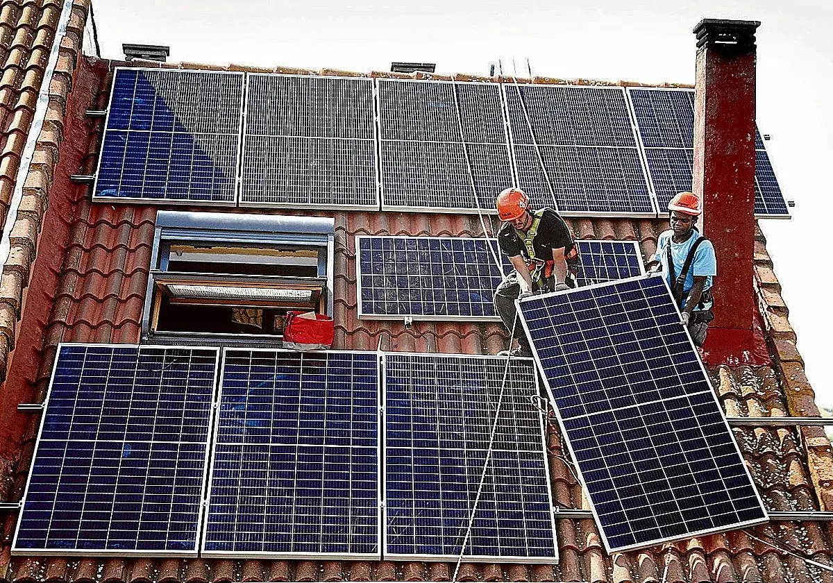 Instalación de placas solares en Extremadura. Dos operarios colocan un panel solar en un tejado, aprovechando la subvención.
