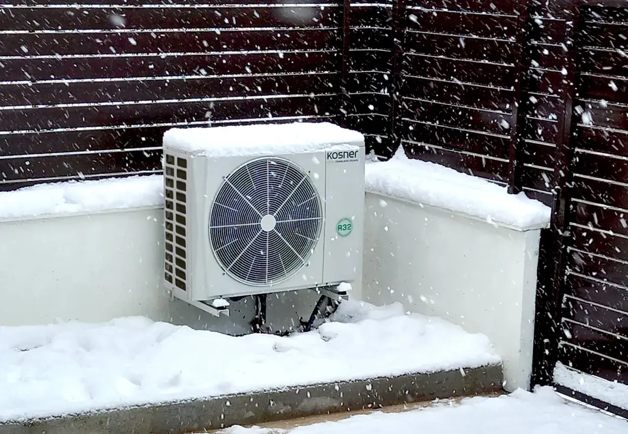 Unidad exterior de bomba de calor Kosner cubierta de nieve, mostrando su capacidad para mantener la temperatura en invierno.