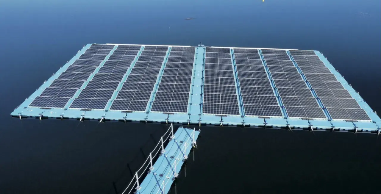 Plataforma de energía fotovoltaica flotante sobre un cuerpo de agua azul, con un pasarela azul conectada.