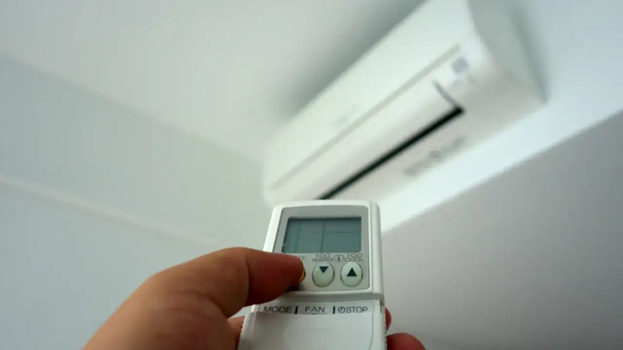Mano con mando a distancia ajustando el aire acondicionado. Averigua cuanto gasta un aire acondicionado por hora para ahorrar energía.