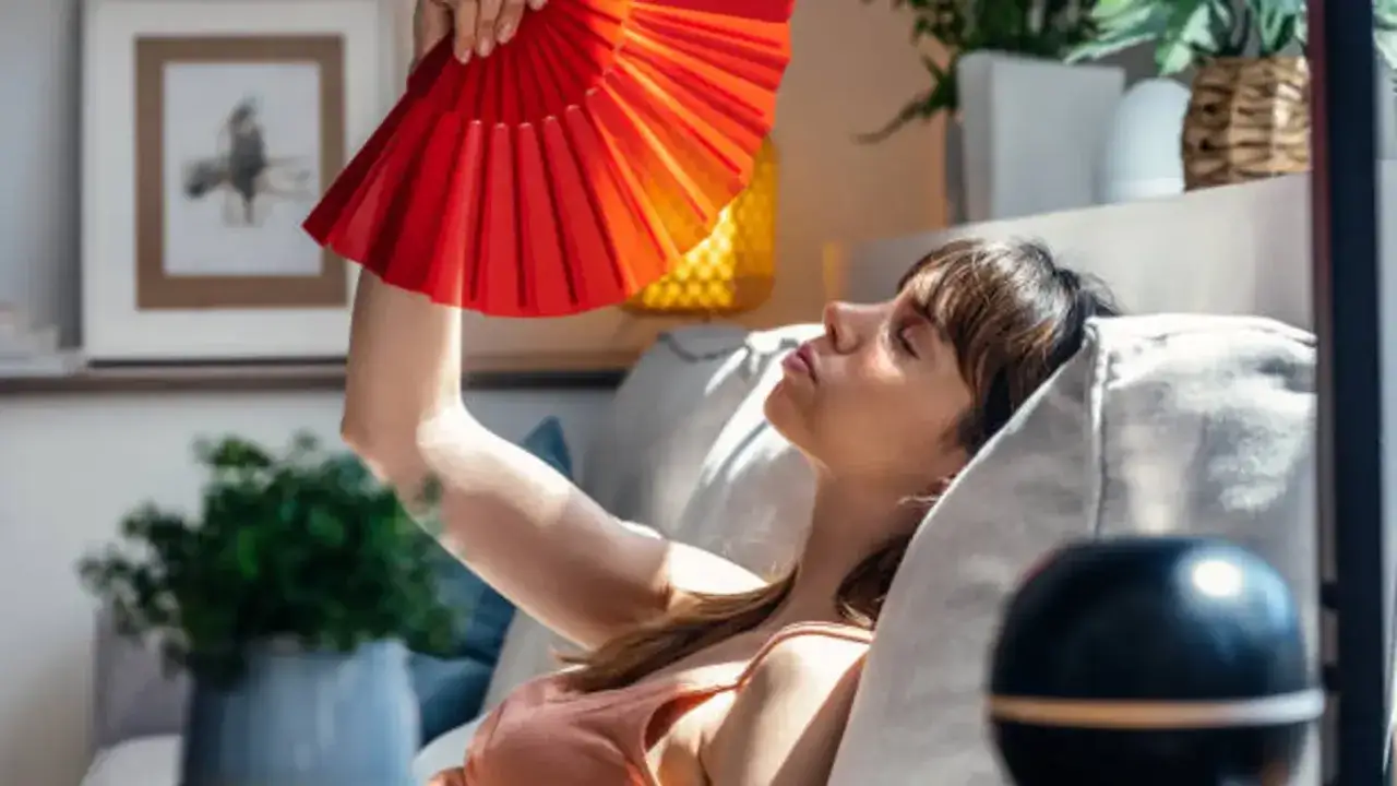 Mujer abanicándose con un abanico rojo para combatir el calor en un día soleado.