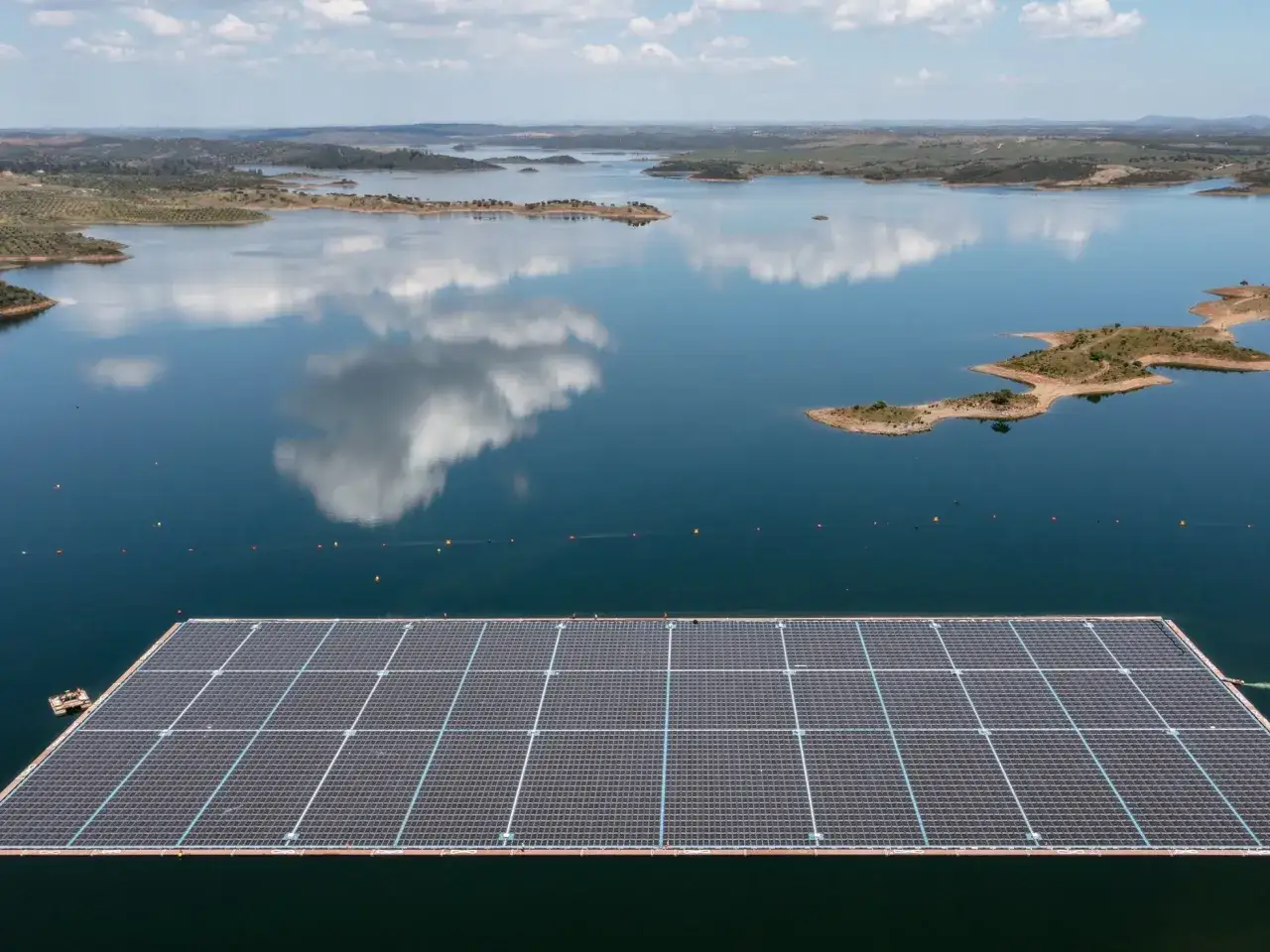 Granja fotovoltaica flotante sobre un embalse, con islas y colinas verdes al fondo.
