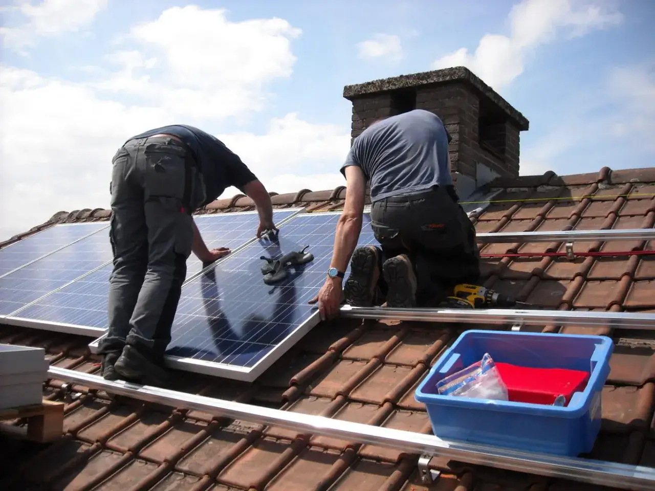 Instalación de paneles solares gratis gobierno. Dos técnicos trabajan en un tejado instalando paneles solares bajo un cielo azul.