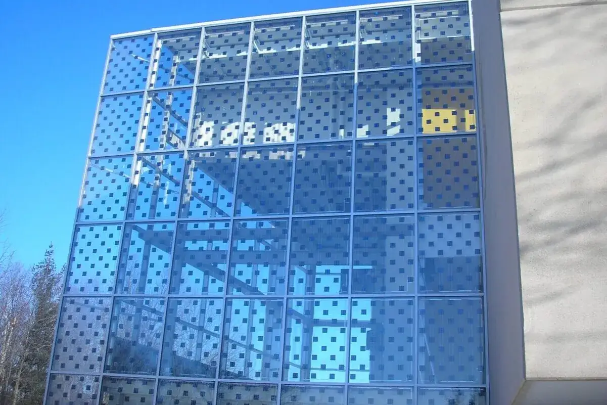 Fachada de edificio moderno con placas solares transparentes integradas en el vidrio, creando un patrón cuadriculado azul.