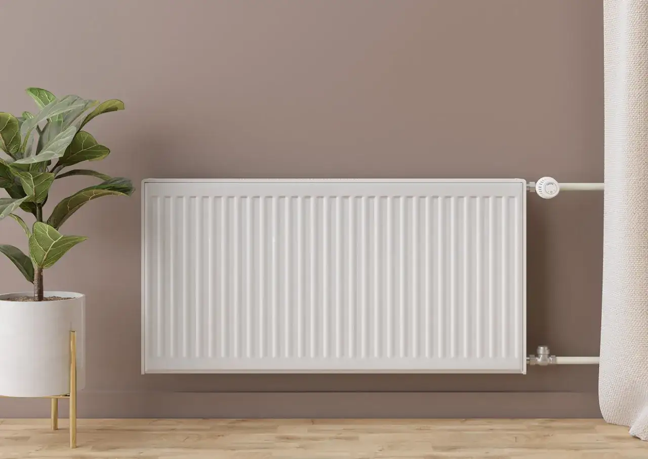 Radiador blanco moderno, parte de un sistema de calefacción por radiadores, junto a una planta y cortinas.