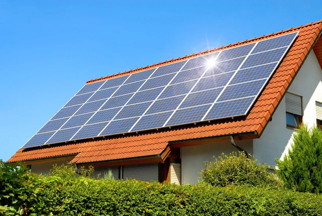 Tejas rojas cubren el tejado de una casa, donde paneles solares captan la luz del sol. Estos son claros usos de la energía solar para un hogar sostenible.