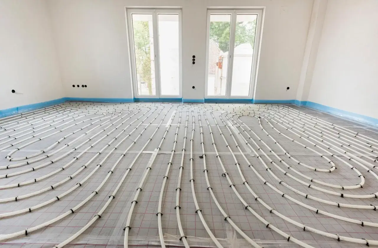 Instalación de tuberías para un futuro suelo radiante en una habitación en construcción, con ventanas al fondo.