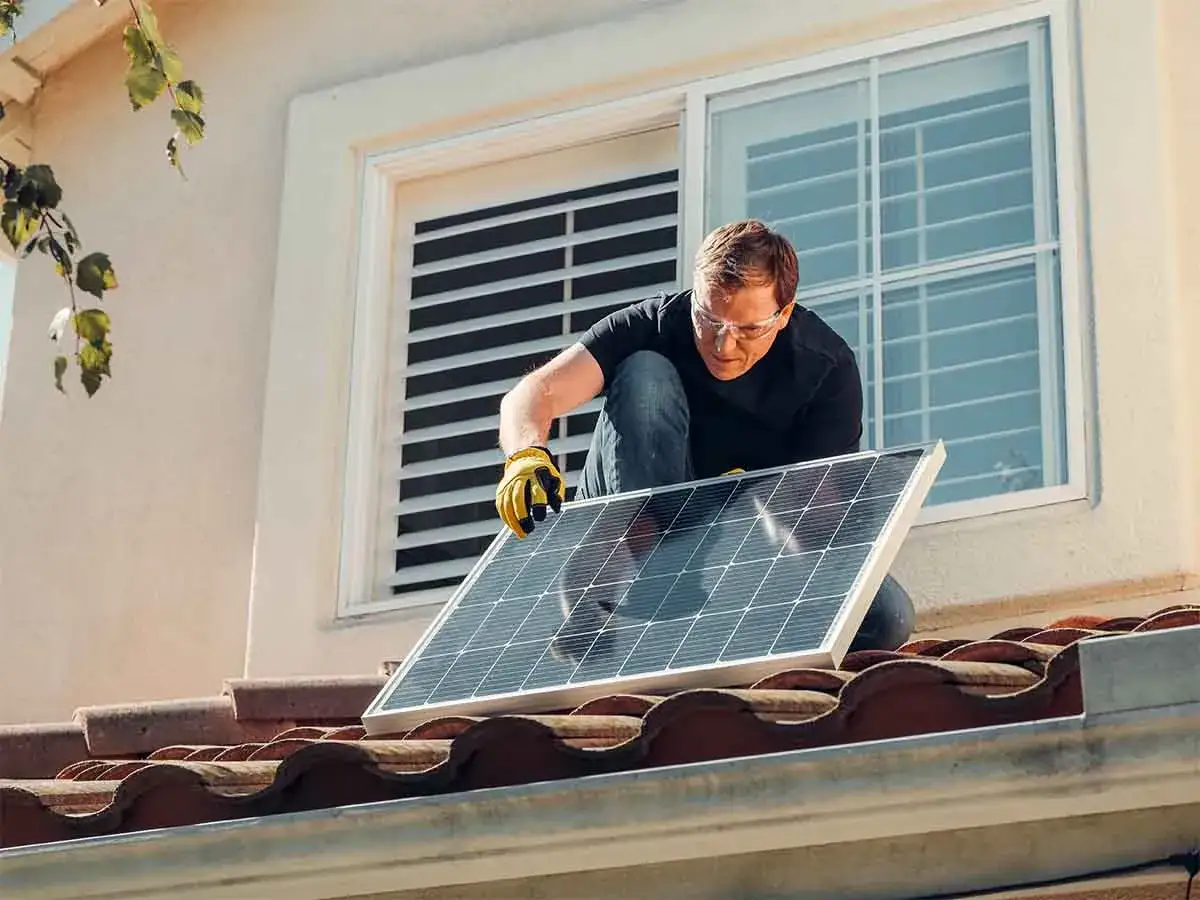 Un hombre instala una placa solar en un tejado, demostrando que se pueden poner placas solares en un piso.