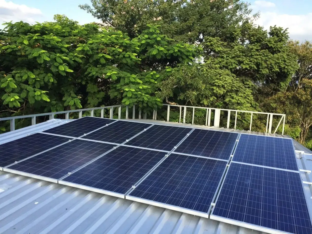 Paneles solares en tejado metálico, rodeados de vegetación exuberante. Una instalación que aprovecha la subvención de placas solares en Extremadura para un futuro más verde.