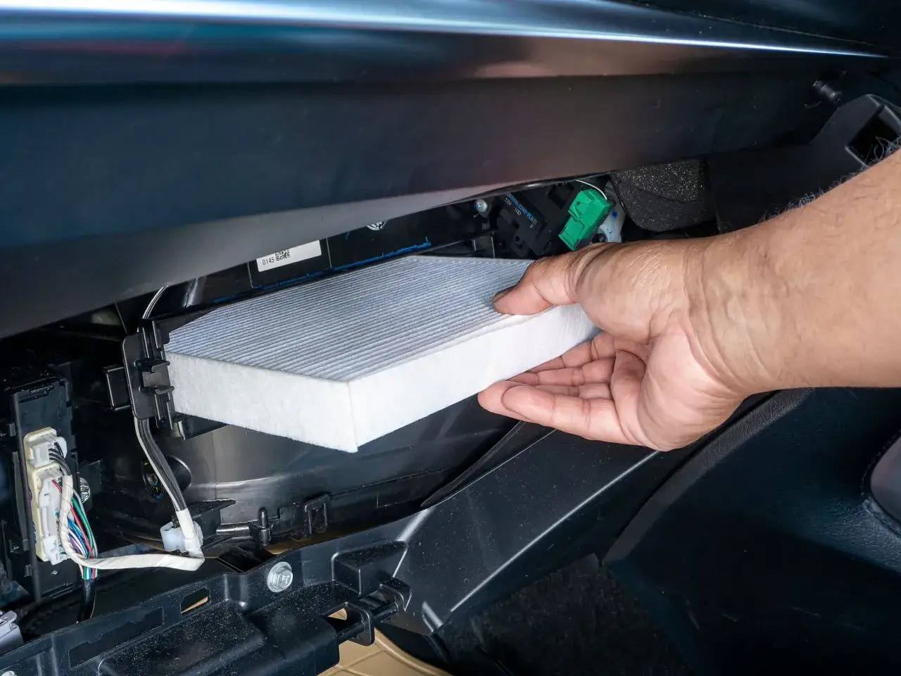 Mano insertando un filtro de aire nuevo en un coche. Pregúntate cada cuanto se cambia el filtro de aire para mantener el aire limpio.
