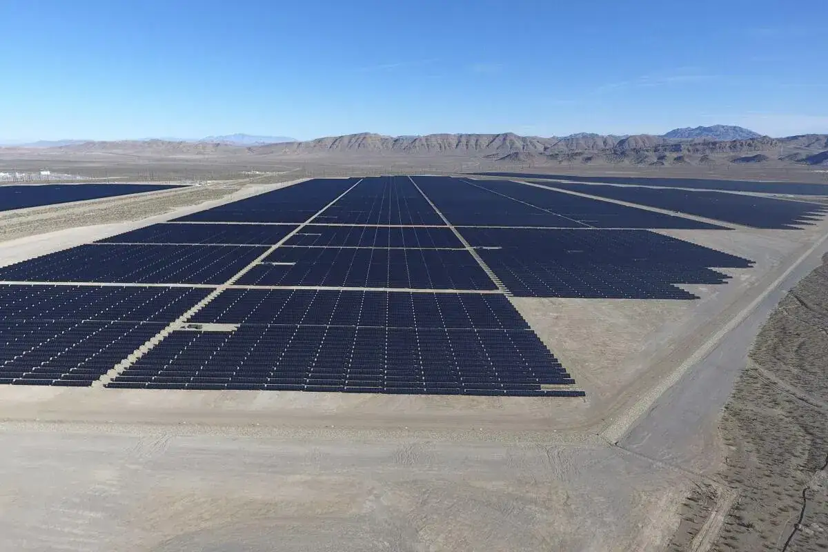 Vasto parque solar en un paisaje desértico, con hileras interminables de paneles oscuros bajo un cielo azul claro.