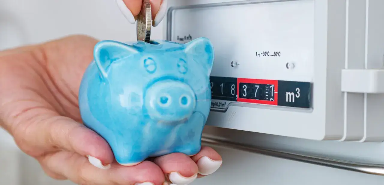 Ahorra para el plan renove calderas. Mano inserta moneda en hucha azul junto a contador de gas.