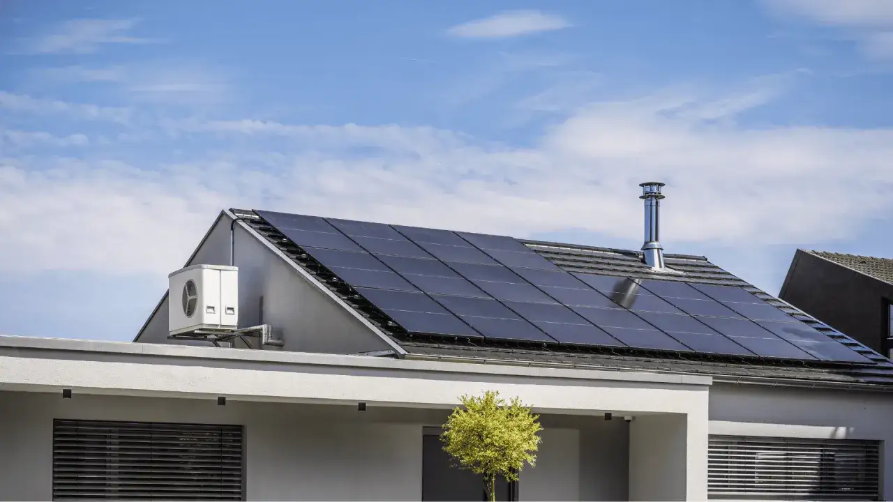 Paneles solares en tejado, ideal para aprovechar el descuento IBI placas solares. Aire acondicionado exterior y chimenea metálica. Cielo azul con nubes.