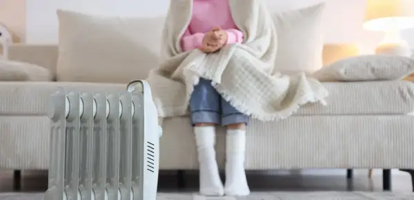 Persona abrigada con manta y calcetines sentada en sofá, junto a un radiador eléctrico. ¿Qué sistema de calefacción elegir para estar cómodo?