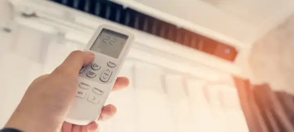 Mano ajustando el control remoto de un aire acondicionado para disfrutar de unas agradables frigorías.
