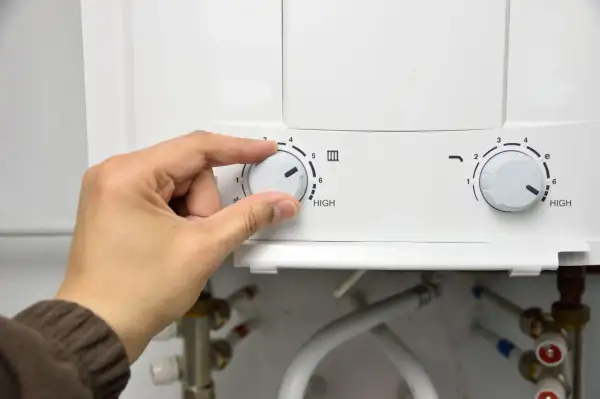 Mano ajustando el dial de temperatura de un termo eléctrico. Se acerca el momento de desmontar el termo eléctrico para su mantenimiento.