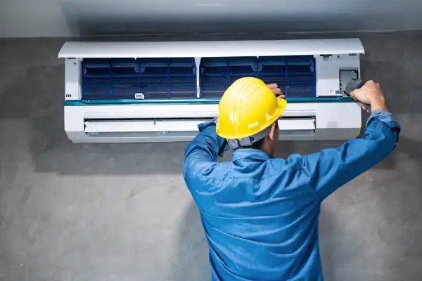 Técnico con casco amarillo ajusta un aire acondicionado, buscando reducir los decibelios del aire acondicionado para un ambiente más silencioso.