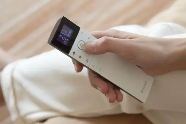 Mano ajustando el control remoto de un cool aire acondicionado a 21 grados.