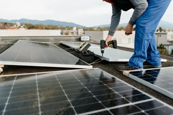 Instalación de un panel solar para aire acondicionado en una azotea. Un técnico usa un taladro para fijar el panel.